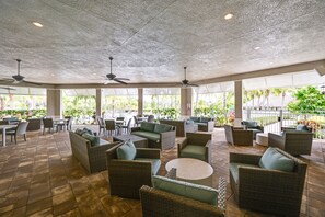Relax in comfort with wicker sofas and armchairs arranged around round tables, surrounded by lush greenery and a serene view.