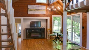 Amplia sala de estar con piso de madera, chimenea, televisor y comedor con mesa de vidrio.