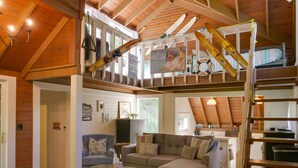Una sala de estar acogedora con un amplio sofá modular, una pequeña mesa de centro y una escalera con esquíes y tablas de snowboard.