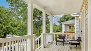 Een overdekt terras met witte hekwerk en twee rieten stoelen met kussens, plus een deurmat.