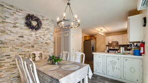 A dining area with a table set for four, surrounded by white chairs, a chandelier, and a decorative wreath on the wall. - Hot Tub, Game Room & Fire Pit: Pocono Summit Home! (Pocono Summit)