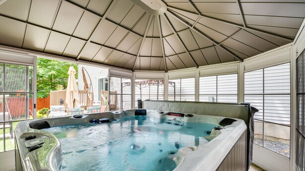 A hot tub under a covered patio with a view of a house and greenery outside. - Hot Tub, Game Room & Fire Pit: Pocono Summit Home! (Pocono Summit)