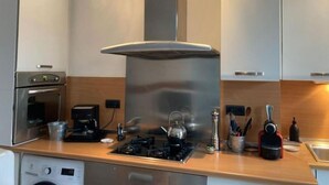 Une cuisine moderne dotée d’appareils électroménagers en acier inoxydable, d’un four encastré, d’une machine à café et d’une bouilloire posées sur le plan de travail.