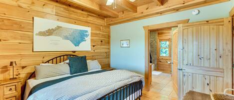 Un dormitorio de cabaña de madera con cama, ventilador de techo, un mapa en la pared y una puerta de madera.