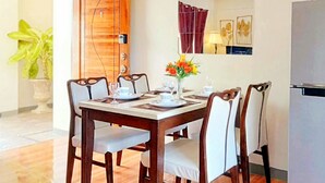 A dining area with a wooden table and chairs, a vase of flowers, and a refrigerator.