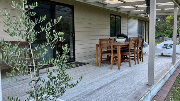 Un patio techado con una mesa y sillas de madera, una planta en maceta y una parrilla.