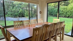 Un comedor con mesa y sillas de madera, ventanas amplias y vistas a un jardín verde.