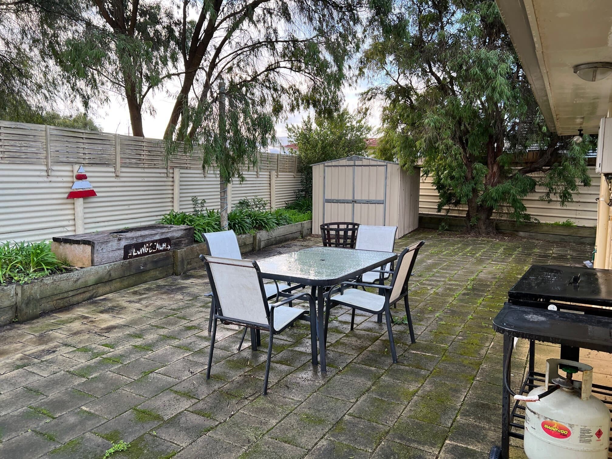 A patio with a table and chairs, a gas cylinder, and a shed.