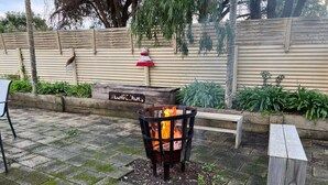 A fire pit in a garden area with a wooden bench and a directional sign.