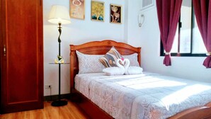 Un dormitorio con cama de madera, ropa de cama blanca, una lámpara de noche y una obra de arte en la pared.