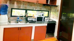 Cocina compacta con estufa a gas, microondas, pileta y muebles color naranja.