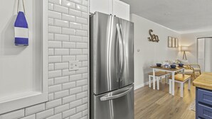 Una cocina moderna con azulejos blancos tipo metro, un refrigerador de acero inoxidable, una mesa de comedor de madera con sillas y una mesita auxiliar.