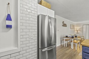 A modern kitchen with white subway tiles, a stainless steel refrigerator, a wooden dining table with chairs, and a small side table.