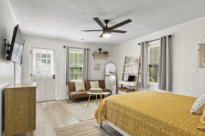 A bedroom with a bed, a desk, a chair, a ceiling fan, and a window with curtains.