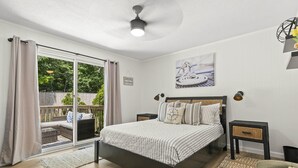 Un dormitorio con cama, mesita de noche, lámpara de pared, ventilador de techo y puerta corrediza de vidrio que da a un espacio exterior.