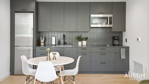 Une cuisine moderne avec des meubles gris, un réfrigérateur en acier inoxydable, un four à micro-ondes et une table de salle à manger ronde avec des chaises blanches.