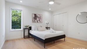 Une chambre à coucher moderne comprenant un lit, une table de chevet, une fenêtre, un ventilateur de plafond et une armoire.