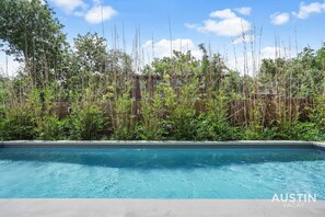 Une piscine rectangulaire à l’eau d’un bleu cristallin, entourée d’une clôture en bambou et d’une végétation luxuriante.