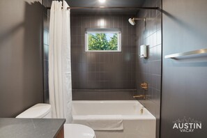 Une salle de bain moderne avec une baignoire, des toilettes et une fenêtre donnant sur les arbres.