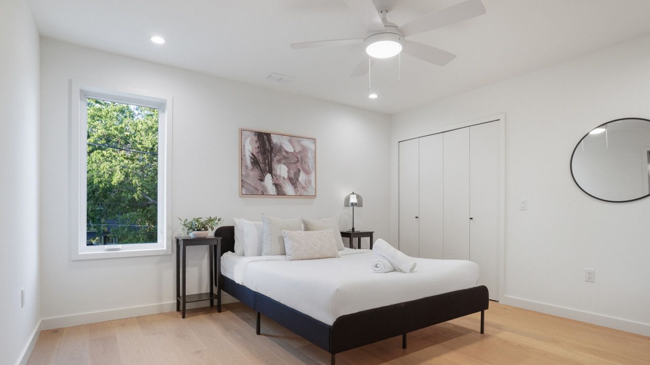 A modern bedroom with a bed, a nightstand, a window, a ceiling fan, and a wardrobe.