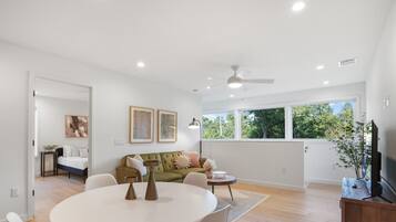 A spacious living room with a round dining table, a green sofa, and a television.