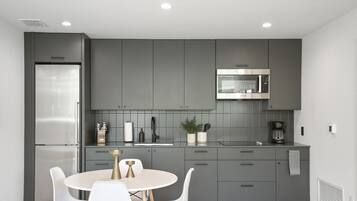 A modern kitchen with grey cabinets, a stainless steel refrigerator, a microwave, and a round dining table with white chairs.
