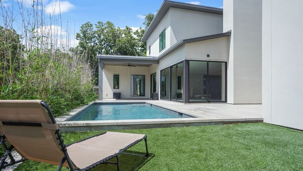 Une maison moderne avec une piscine, une pelouse et une chaise.
