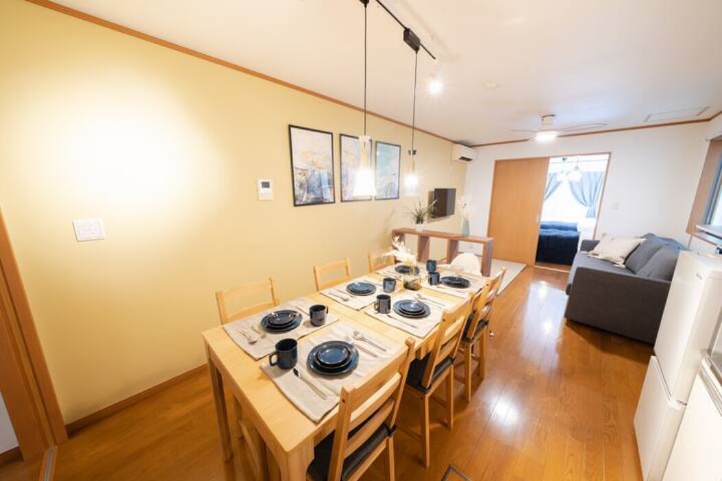 A dining area with a wooden table set for six, chairs, and a kitchen in the background.