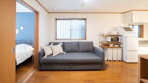 A compact living space with a sofa, a small kitchenette, and a window. - HATAGAYA Apartment 1F (Tokyo)
