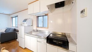 A compact kitchen with white cabinets, a built-in oven, and a window above the sink. - HATAGAYA Apartment 1F (Tokyo)