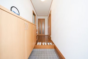 A narrow hallway with a wooden cabinet on the left, a tiled floor, and a door at the end. - HATAGAYA Apartment 1F (Tokyo)