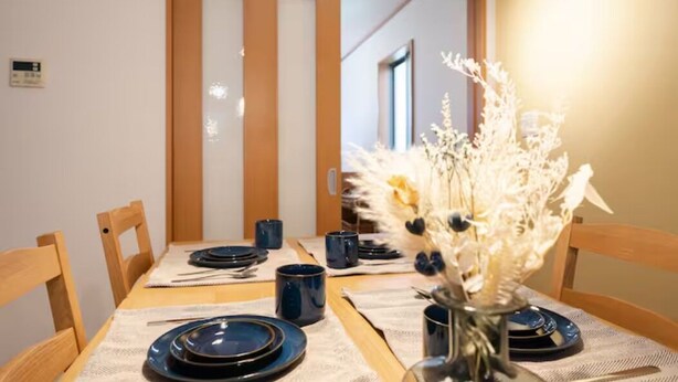 A dining table set with plates, cutlery, and blue cups, with a vase of dried flowers in the center. - HATAGAYA Apartment 1F (Tokyo)