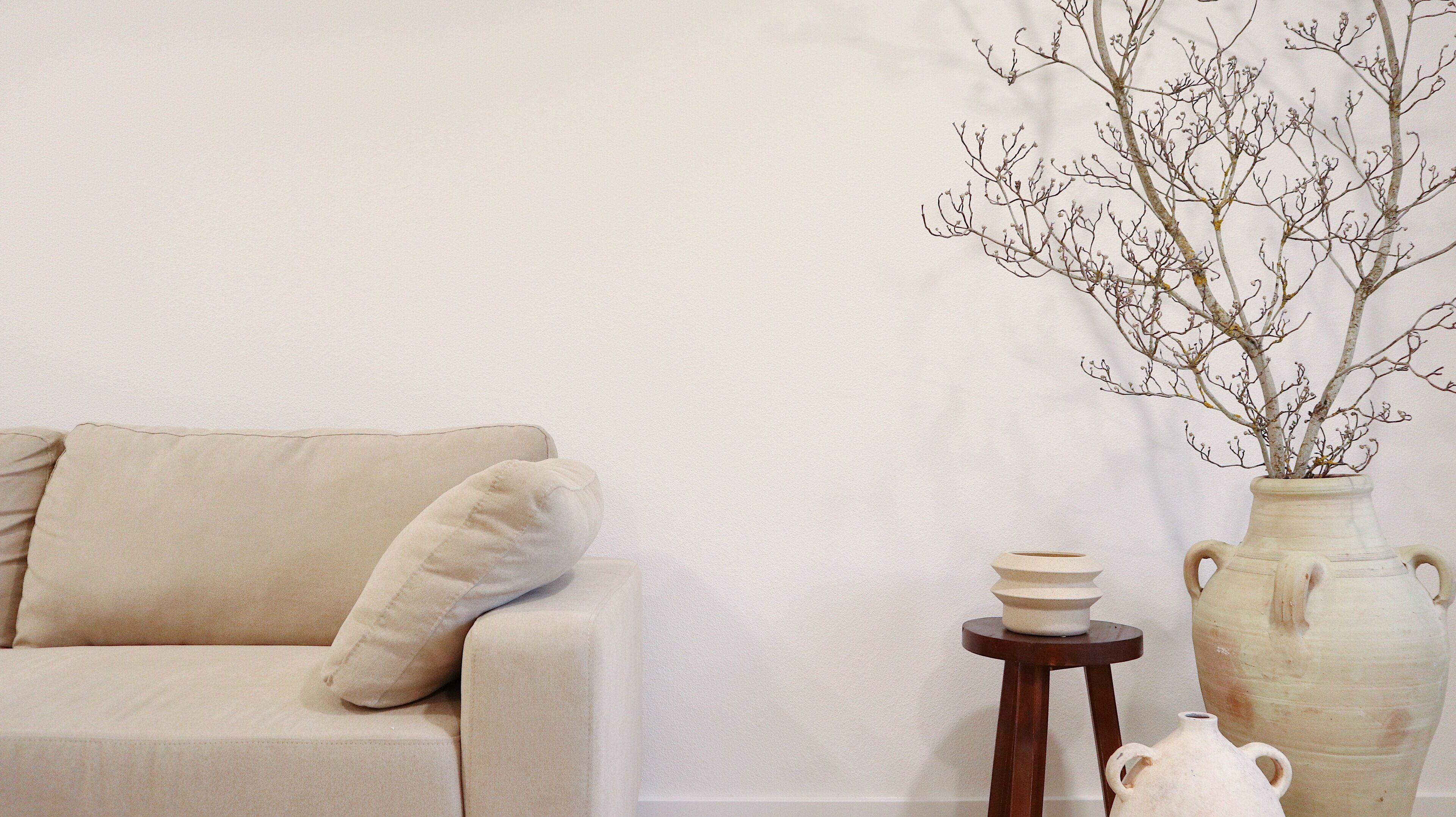A minimalist living room with a beige sofa, a small wooden stool, and a white vase with branches.