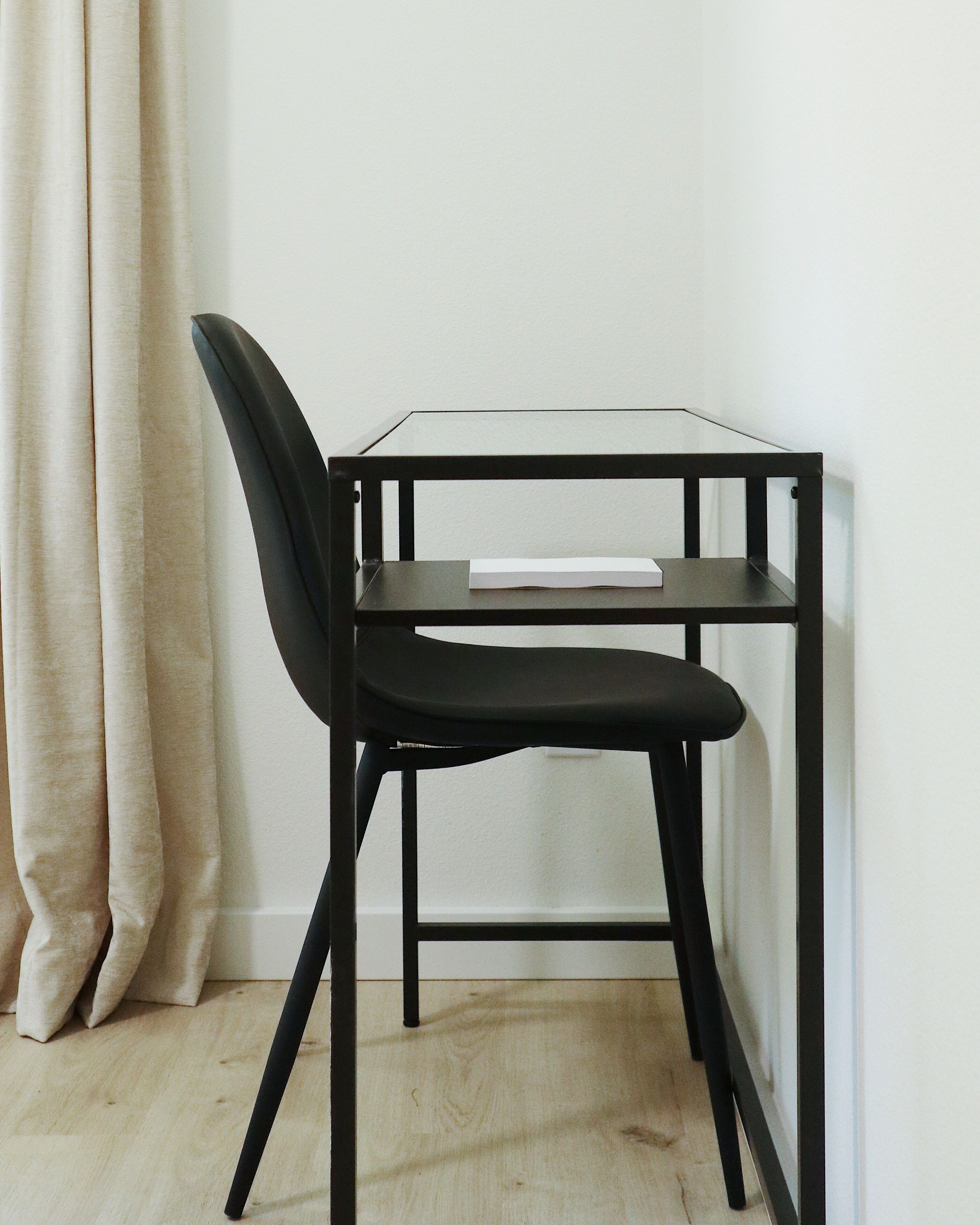 Uma cadeira preta com assento e encosto acolchoados, colocada ao lado de uma pequena mesa preta com tampo de vidro.