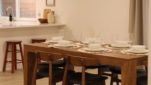 Un comedor con una mesa de madera dispuesta para cuatro, una zona de cocina con ventana y un suelo de tonos claros.
