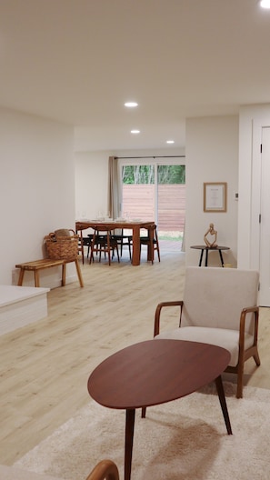 Un vaste espace de vie comprenant une table à manger en bois, préparée pour quatre personnes, un fauteuil confortable et une petite table ronde sur laquelle est posée une sculpture.