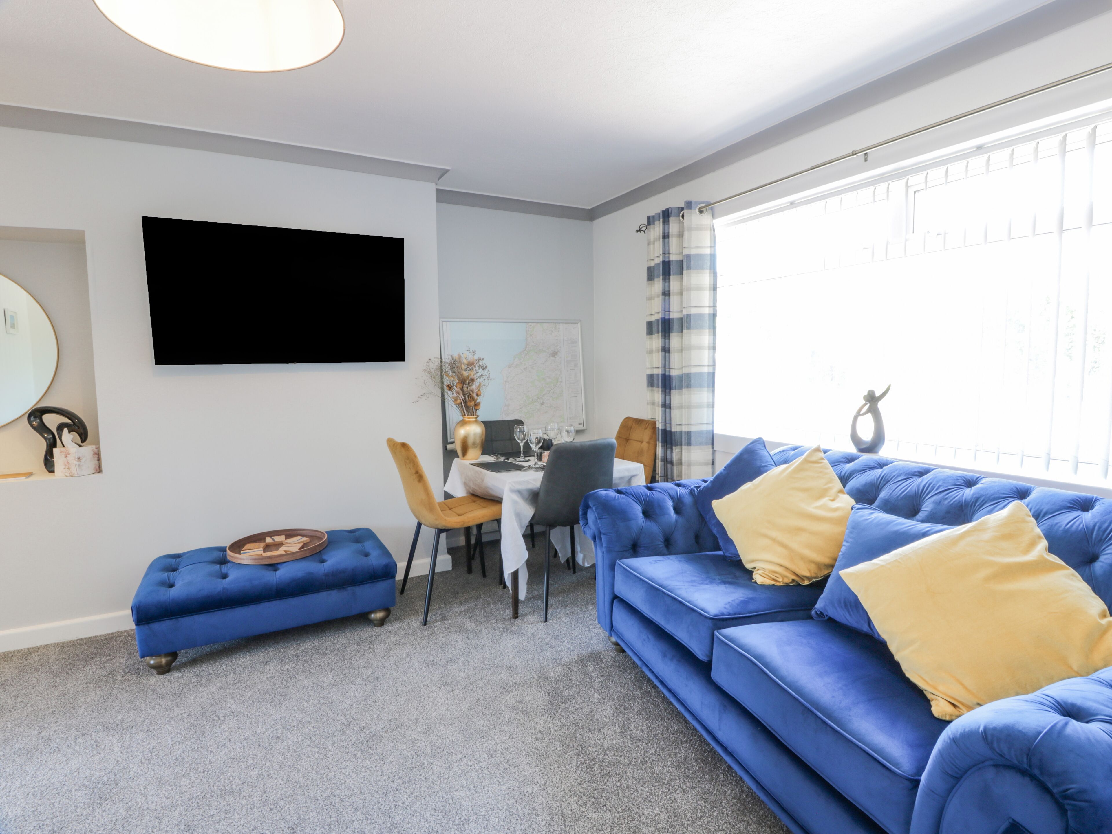 A modern living room with a blue sofa, a small round table, and a flat-screen TV mounted on the wall.