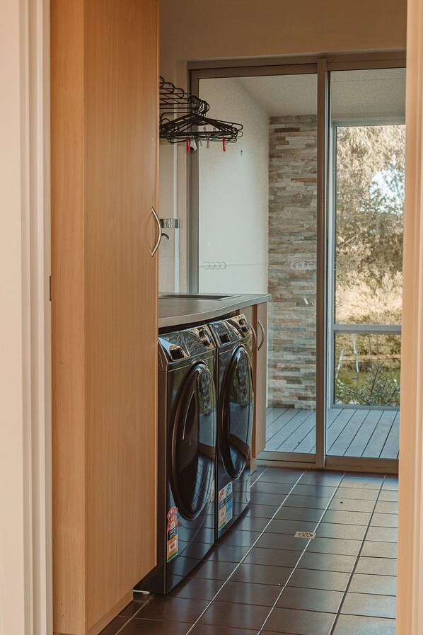 A laundry room with a washing machine and dryer, a wooden cabinet, and a sliding glass door leading to an outdoor area. - 20% Off Weekly | Lagoon-View Summit House | 4BR (Pelican Lagoon)