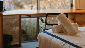 Une chambre à coucher avec un lit, un bureau et une chaise. Il y a une fenêtre qui donne sur les arbres.