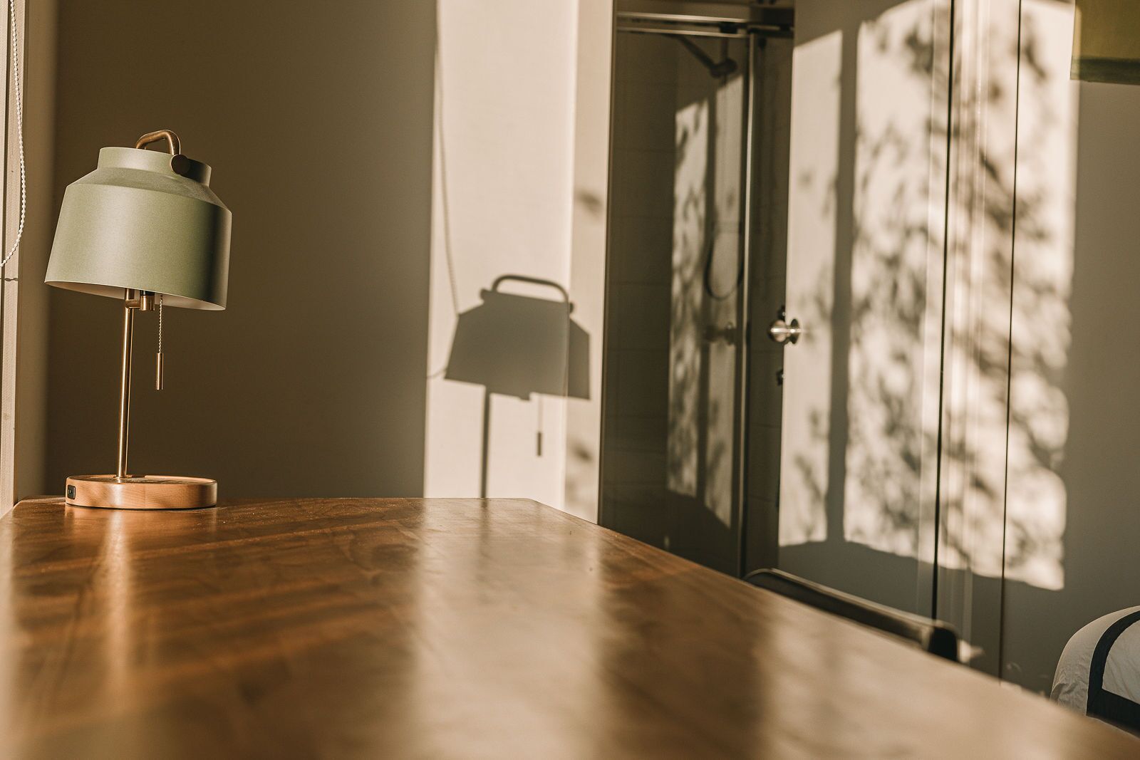Una mesa de madera, una lámpara, una puerta con sombra y una pared.
