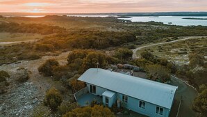 Une maison de plain-pied, dotée d’un toit en pente, entourée d’un paysage naturel avec des arbres et un plan d’eau en arrière-plan.
