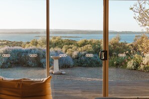 A room with a large window overlooking a garden with a birdbath and a view of the sea. - 20% Off Weekly | Lagoon-View Summit House | 4BR (Pelican Lagoon)