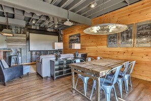 A rustic interior with a wooden dining table, metal chairs, a sofa, and a projector screen.