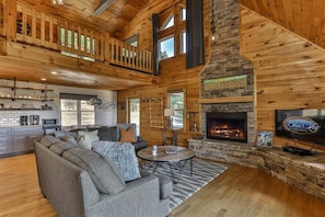 A spacious living area with a fireplace, a television, and a kitchen in the background.