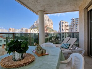 A balcony with a table set for two, a potted plant, and a view of a mountain and cityscape. - A88 EDIFICIO LARIMAR 8-D (Calpe)