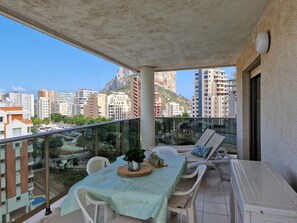 A balcony with a table set for two, overlooking a cityscape with buildings and a mountain. - A88 EDIFICIO LARIMAR 8-D (Calpe)