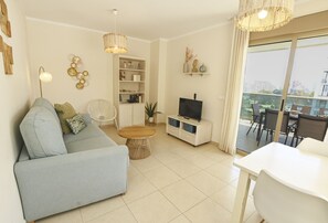 Ein Wohnzimmer mit Sofa, Fernseher, Esstisch und Balkon mit Sitzgelegenheit.