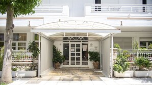 Entrada de un hotel con un paseo techado, plantas en macetas y acceso empedrado.