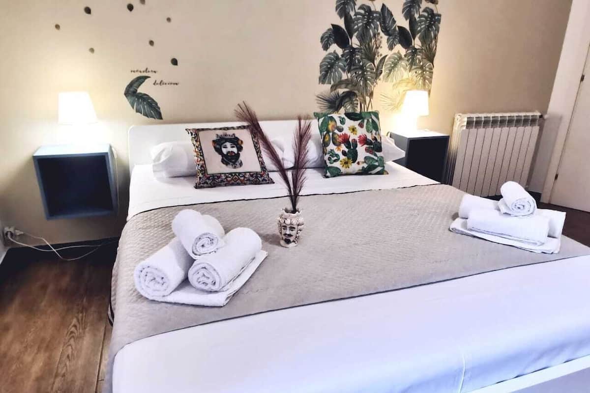 Una cama bien hecha con toallas enrolladas, un jarrón decorativo y un cuadro en la cabecera.