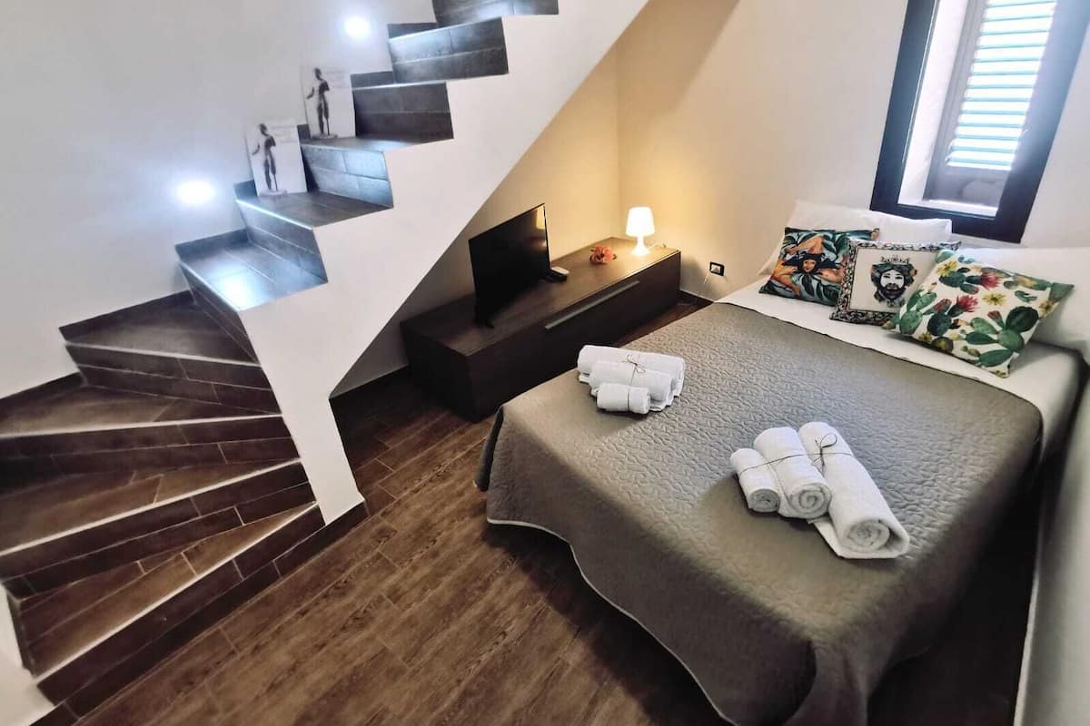 Un dormitorio con cama, mesita de noche, televisor y escalera.